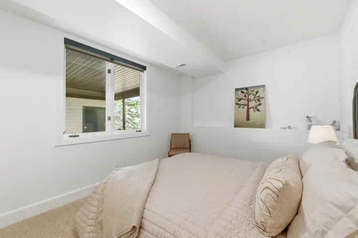 Bedroom with light-colored carpeting, white baseboards, and a window with a dark roller shade