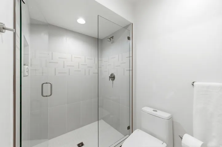 Walk-in shower featuring a frameless glass enclosure, a tiled accent band with a geometric pattern, recessed lighting, and a brushed nickel shower head