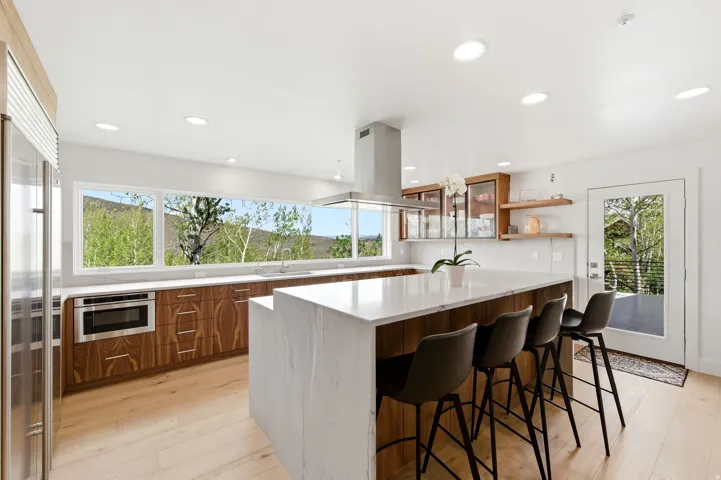 Modern kitchen featuring a large waterfall island with seating, a stainless steel range hood, built-in microwave, and wood-finish cabinetry