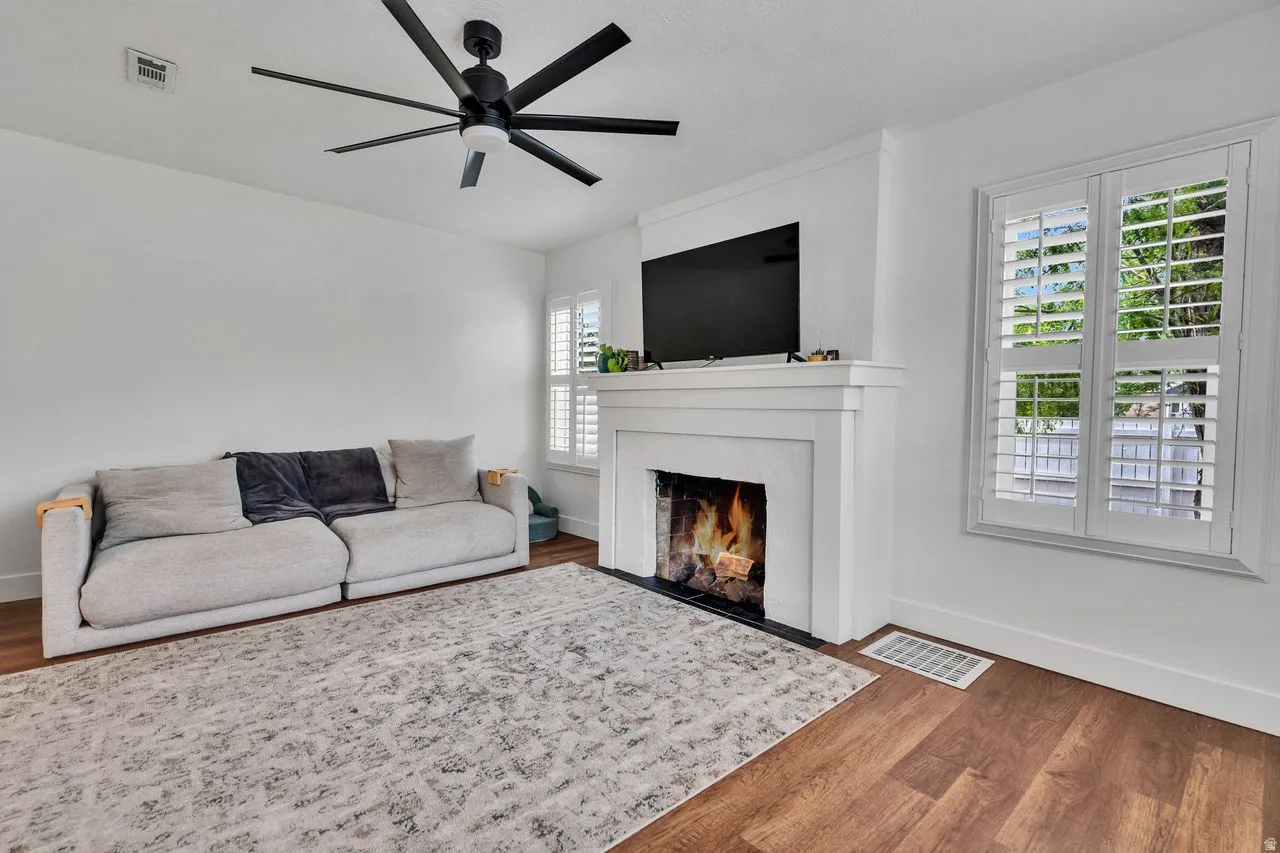 Living area featuring wood-finish flooring, a white fireplace with a black hearth, and plantation shutters