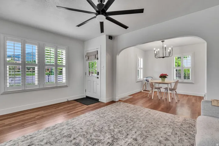 Living area featuring wood-finish flooring, a white paneled entry door, and a multi-pane window with plantation shutters