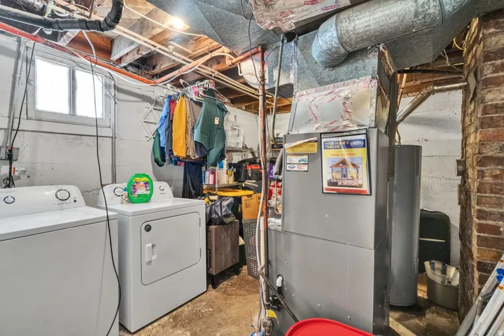 Laundry area featuring white appliances, a small window, exposed ceiling joists, and a brick support structure