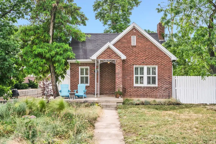 Brick facade home featuring a prominent gabled entry, white window shutters, a front porch, and a white picket fence