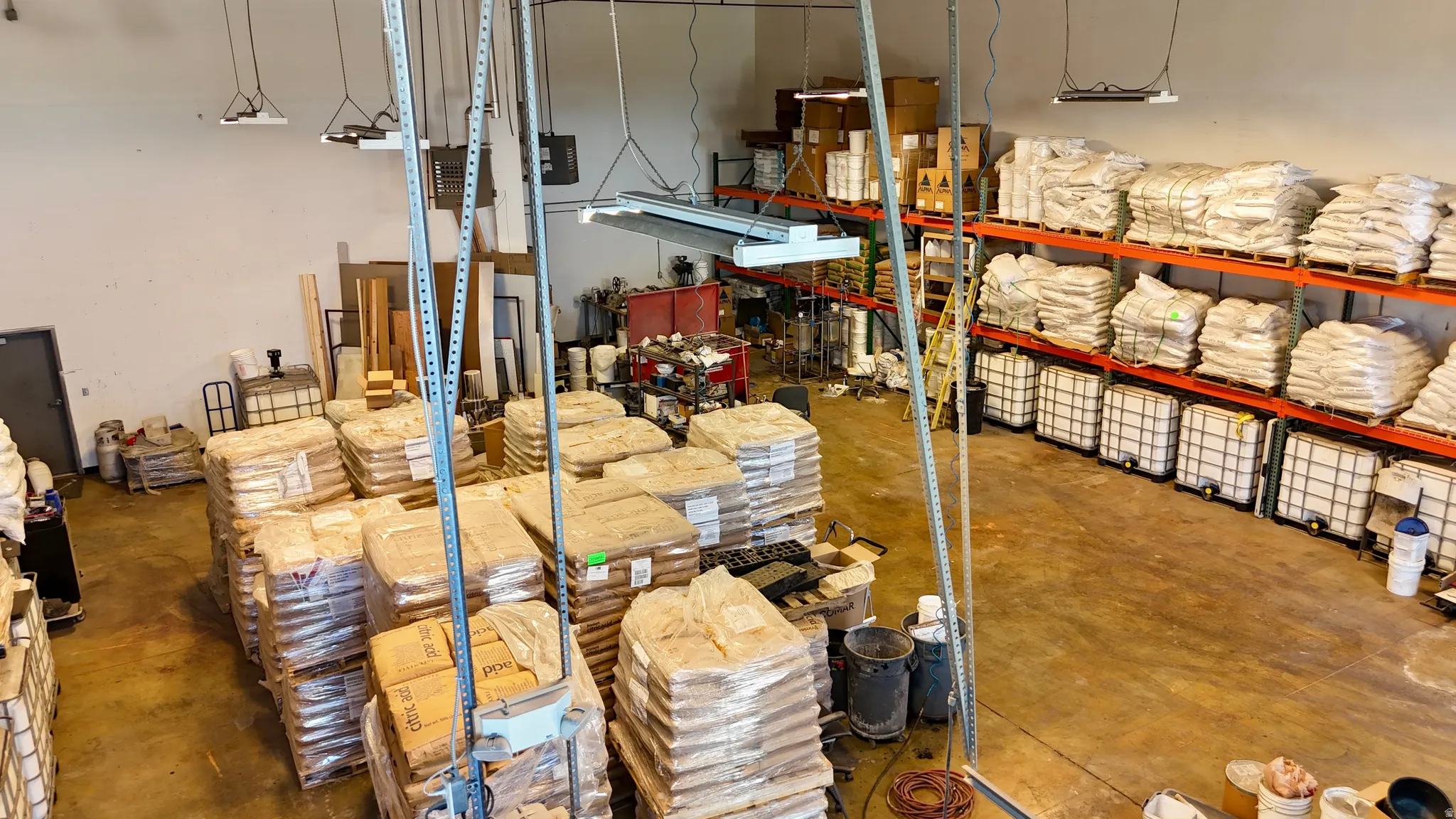 Spacious warehouse interior featuring high ceilings, fluorescent lighting, concrete flooring, and extensive built-in shelving systems
