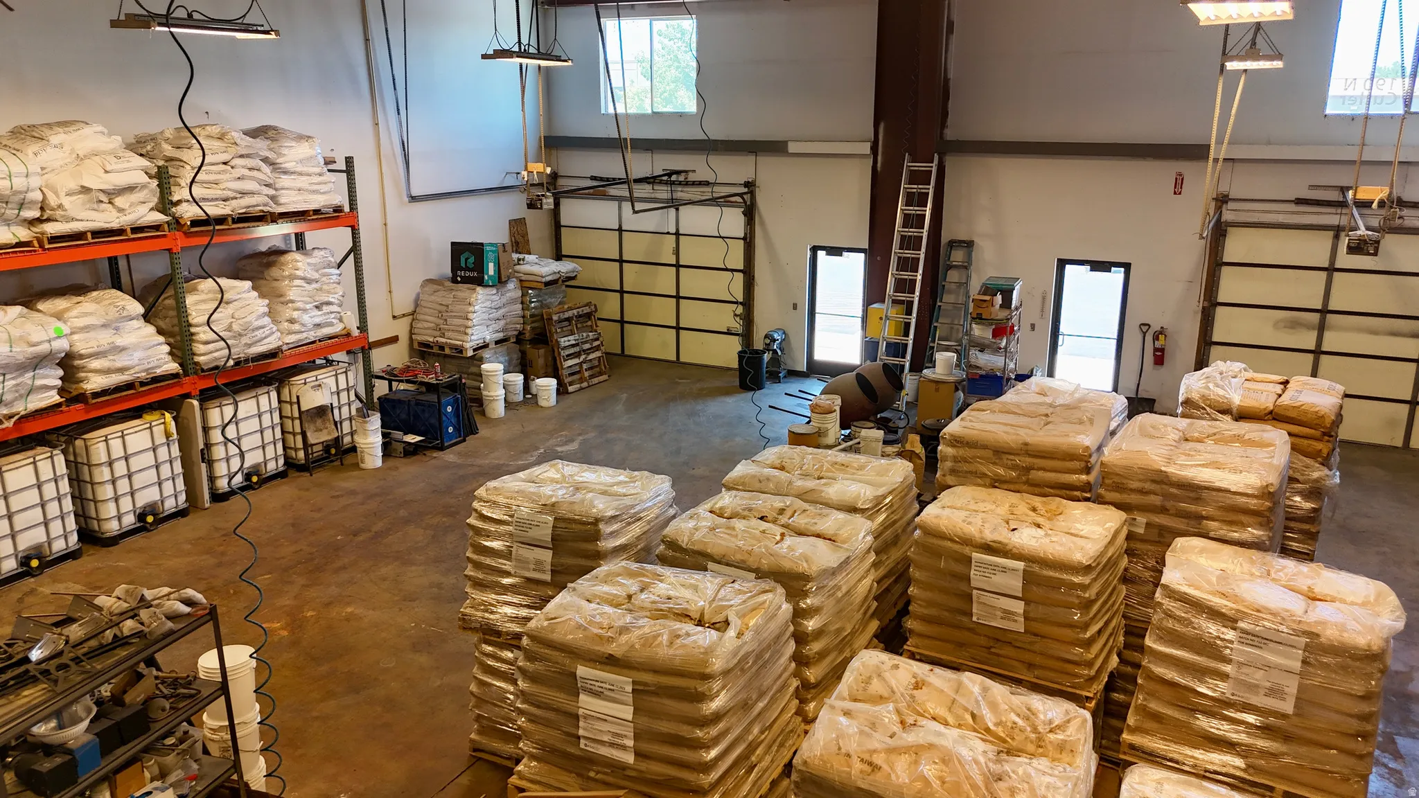 Spacious warehouse interior featuring high ceilings, exposed structural beams, multiple overhead doors, and industrial lighting fixtures