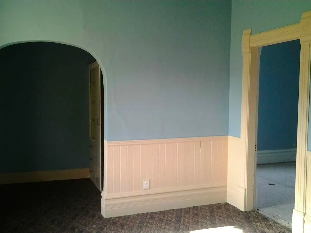 Interior room with blue walls, white wainscoting, and decorative wood trim around a doorway