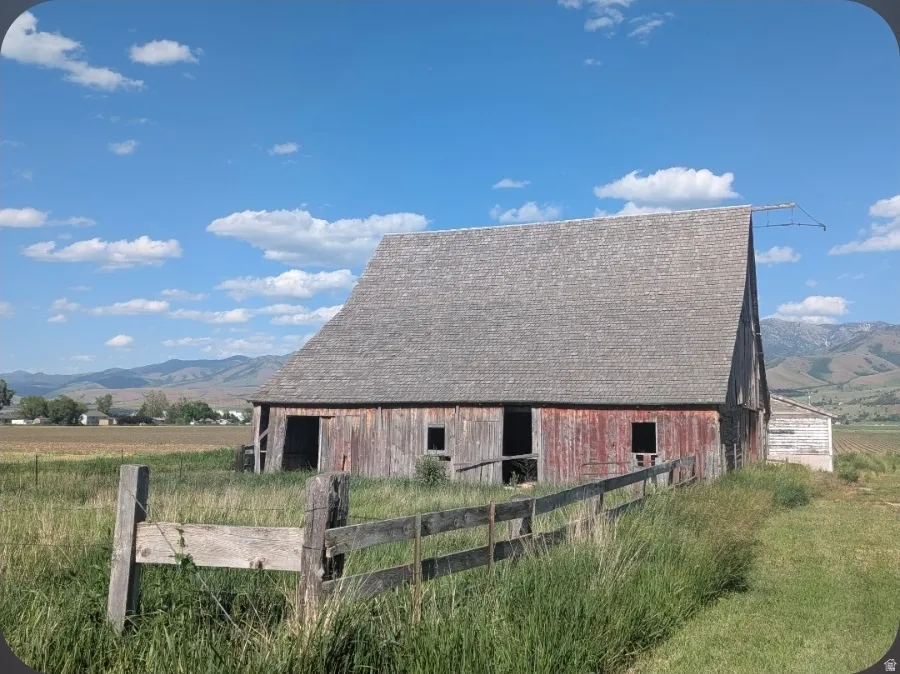 Rustic gambrel-roof barn with faded red siding and multiple openings, surrounded by tall grasses and a wooden fence