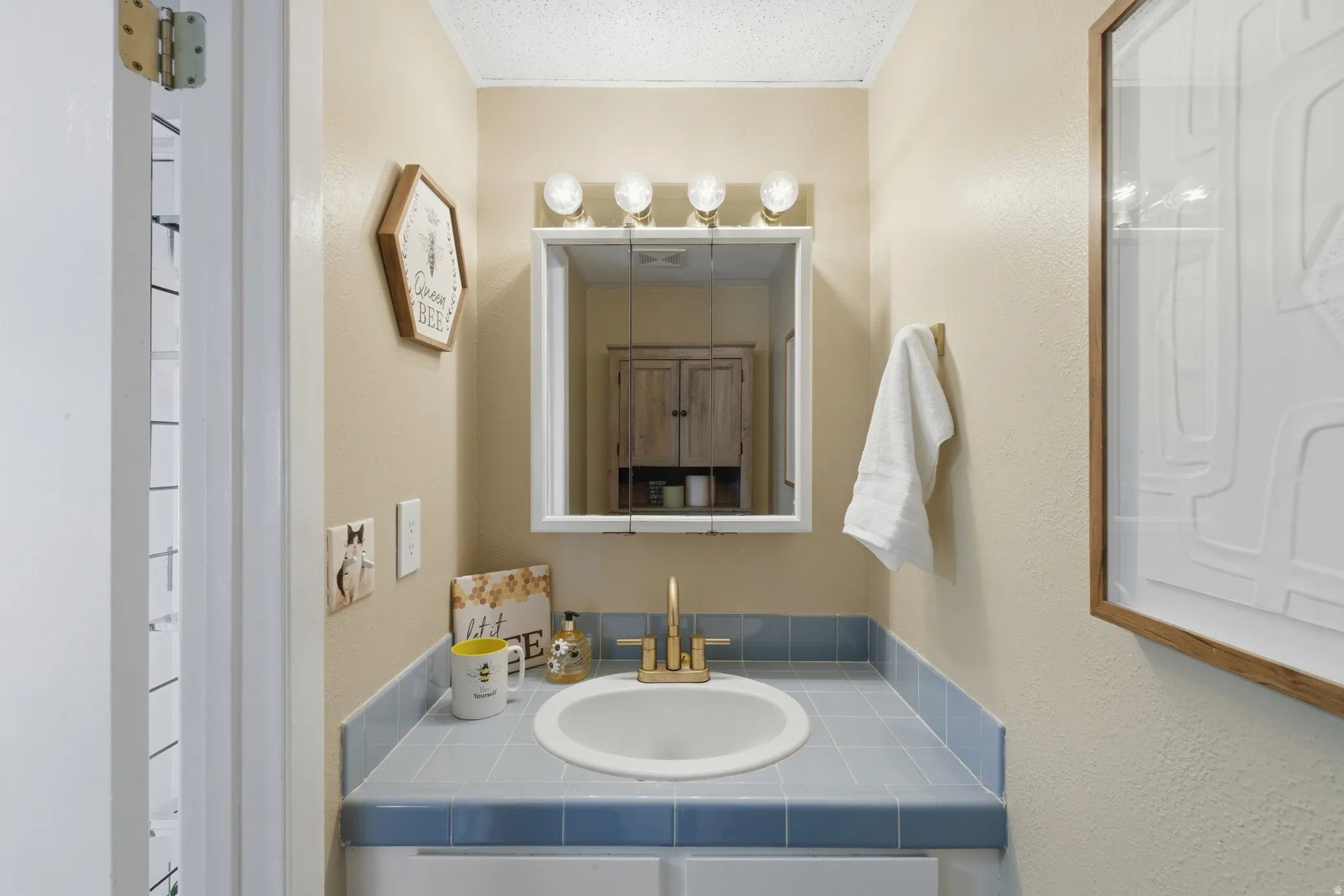 Half Bath witwh vanity featuring a tiled countertop, undermount sink, and a mirrored medicine cabinet with integrated lighting