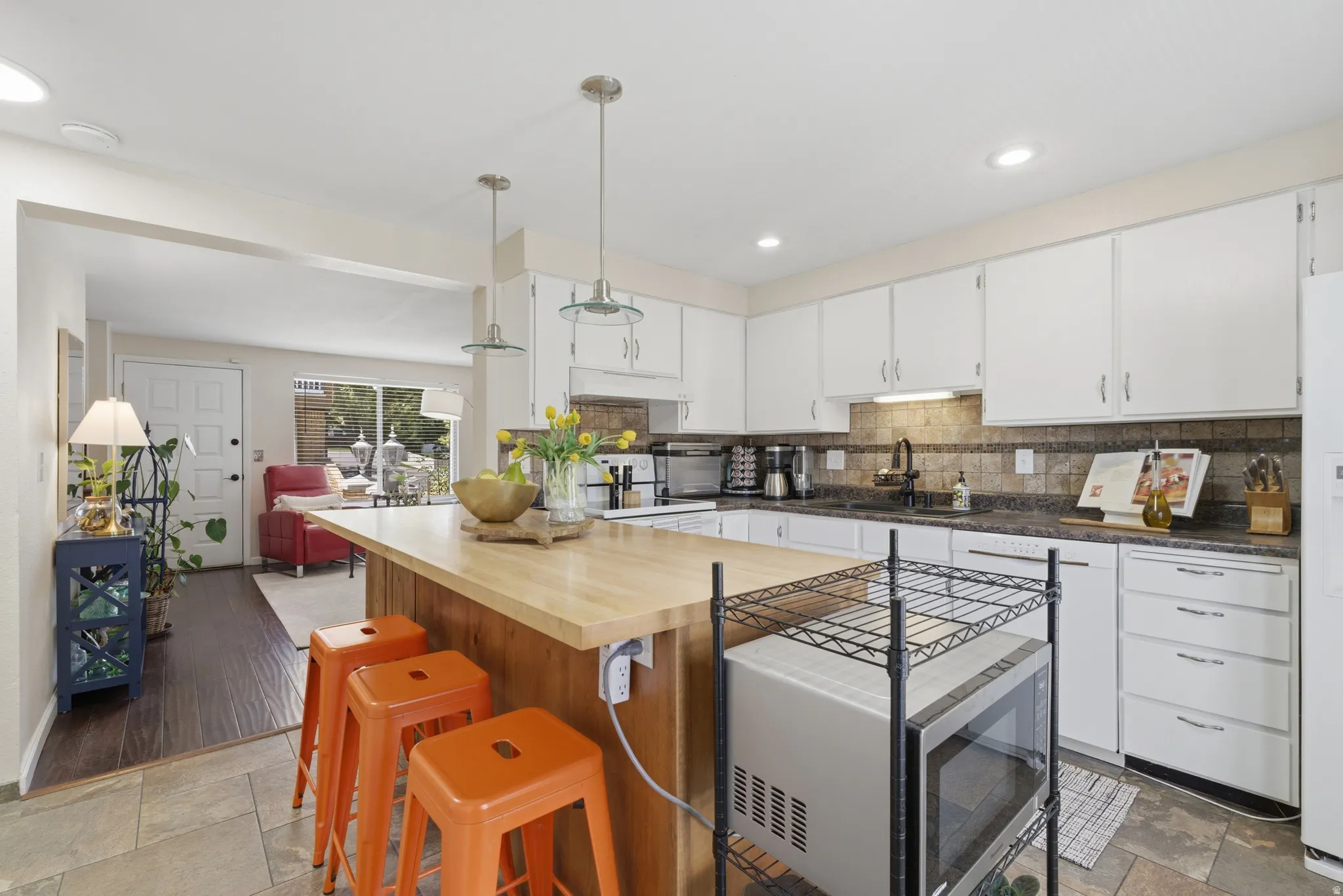 Kitchen featuring a light wood-finish island with pendant lighting, white cabinetry, dark countertops, and a neutral tile backsplash