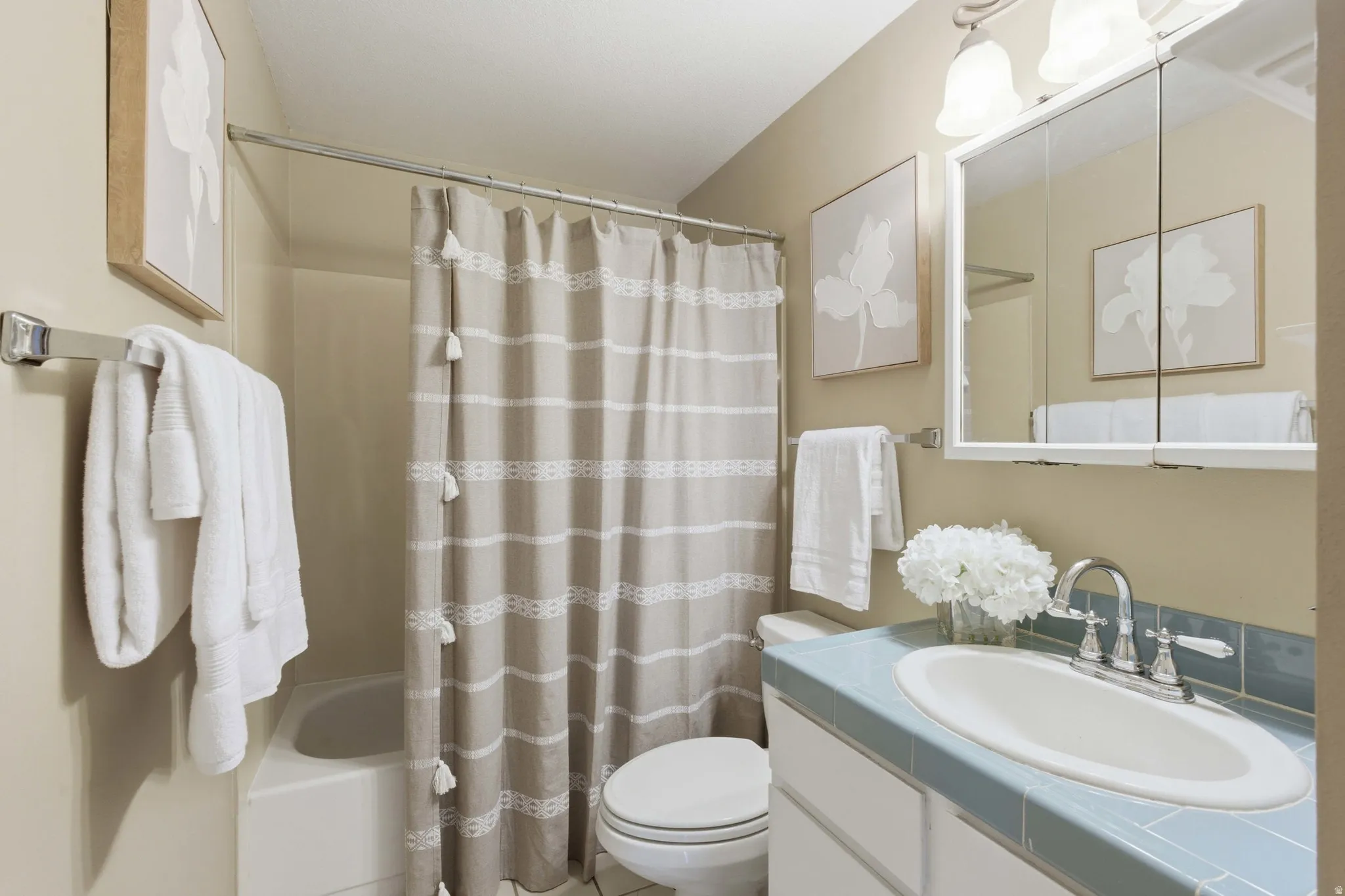 Full bathroom featuring a white tub, shower with chrome rod, white toilet, and a vanity with a white basin sink and light blue countertop