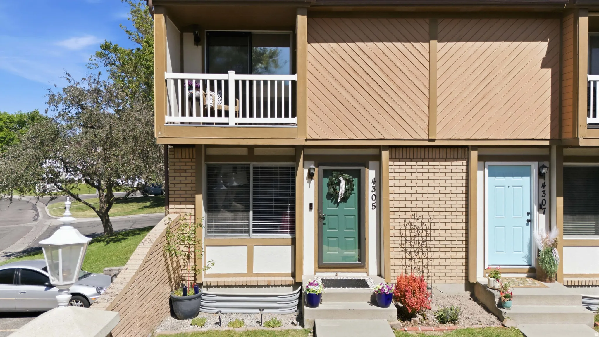 Townhome exterior featuring a private balcony with white railings, a green paneled entry door, and light brown siding with diagonal accents