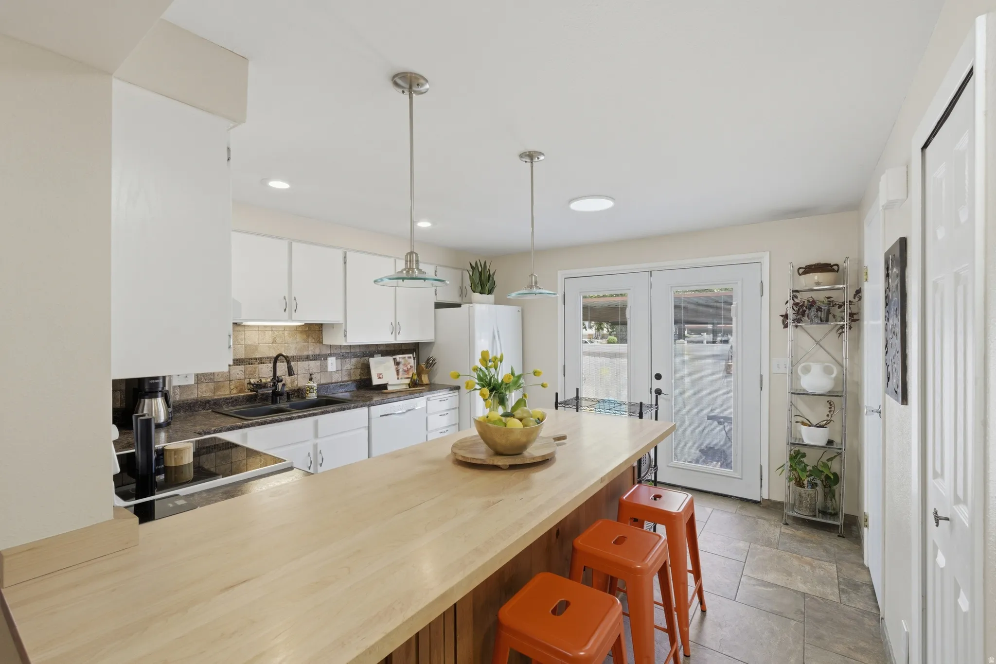 Kitchen featuring a large wood-finish island, white cabinetry, dark countertops, and a tiled backsplash