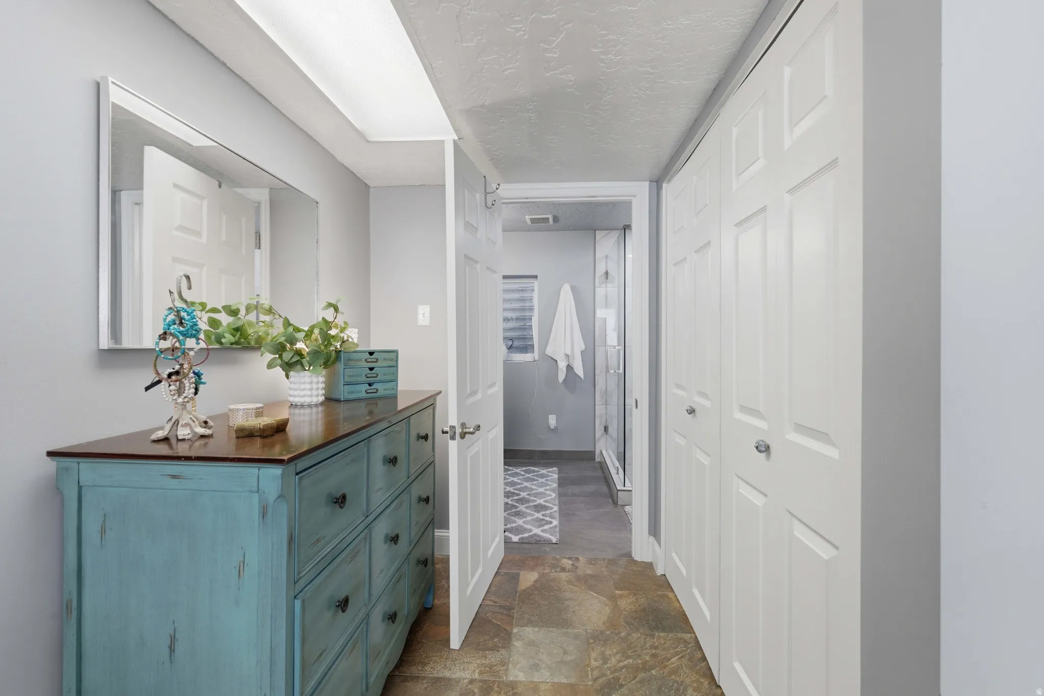 Hallway featuring slate tile flooring, white bi-fold doors to primary closet and ensuite bathroom entrance with a glass-enclosed shower