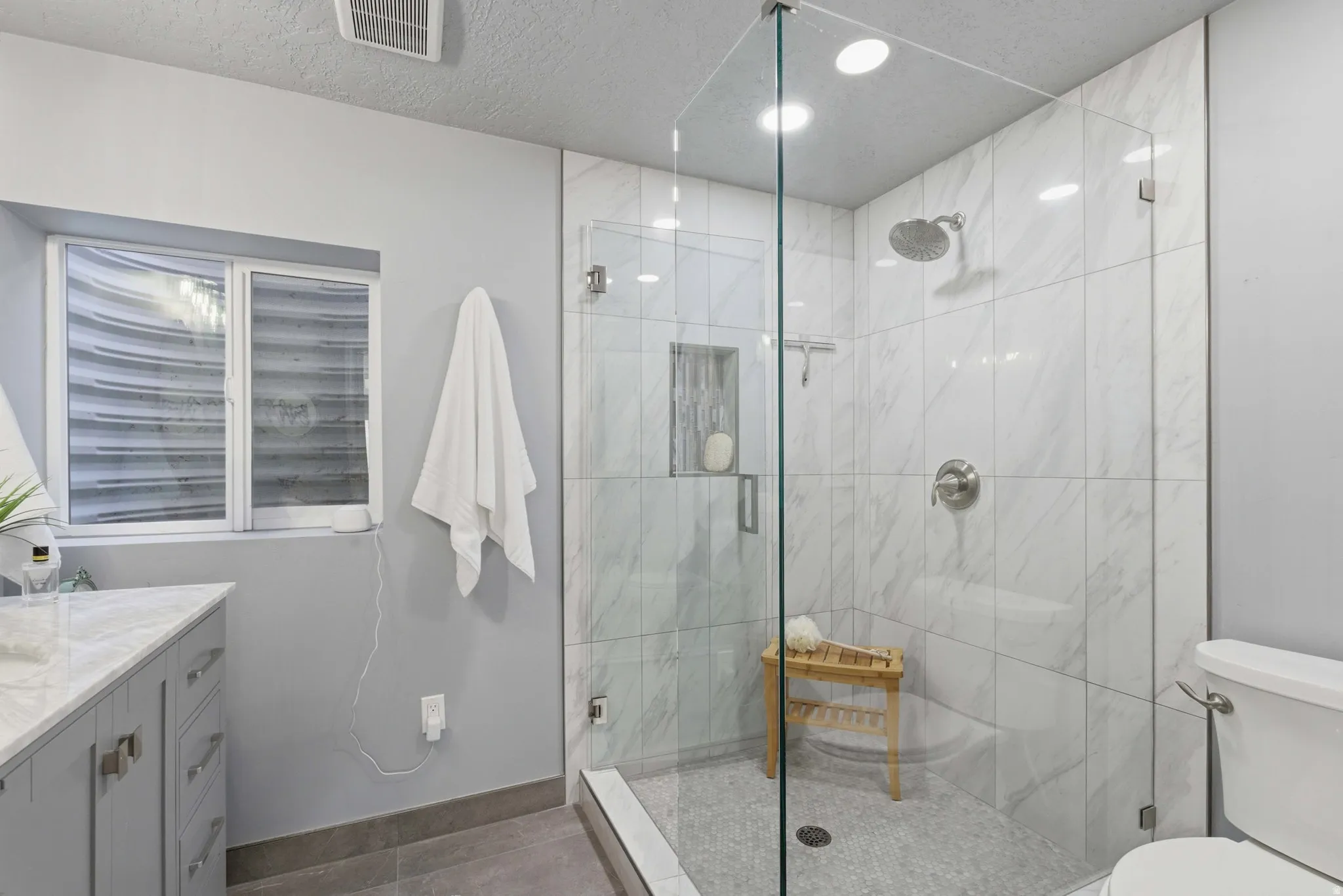 Spacious bathroom featuring a glass-enclosed shower with white marble-finish tile, recessed niche, and a rain showerhead
