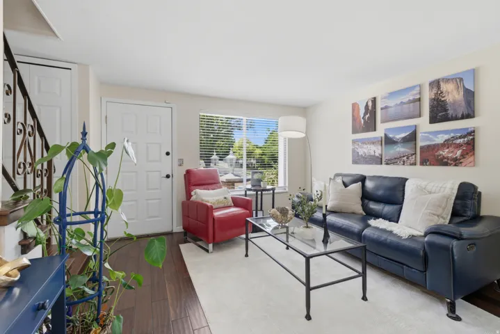 Living area featuring wood flooring, light-toned walls, and a large window with blinds