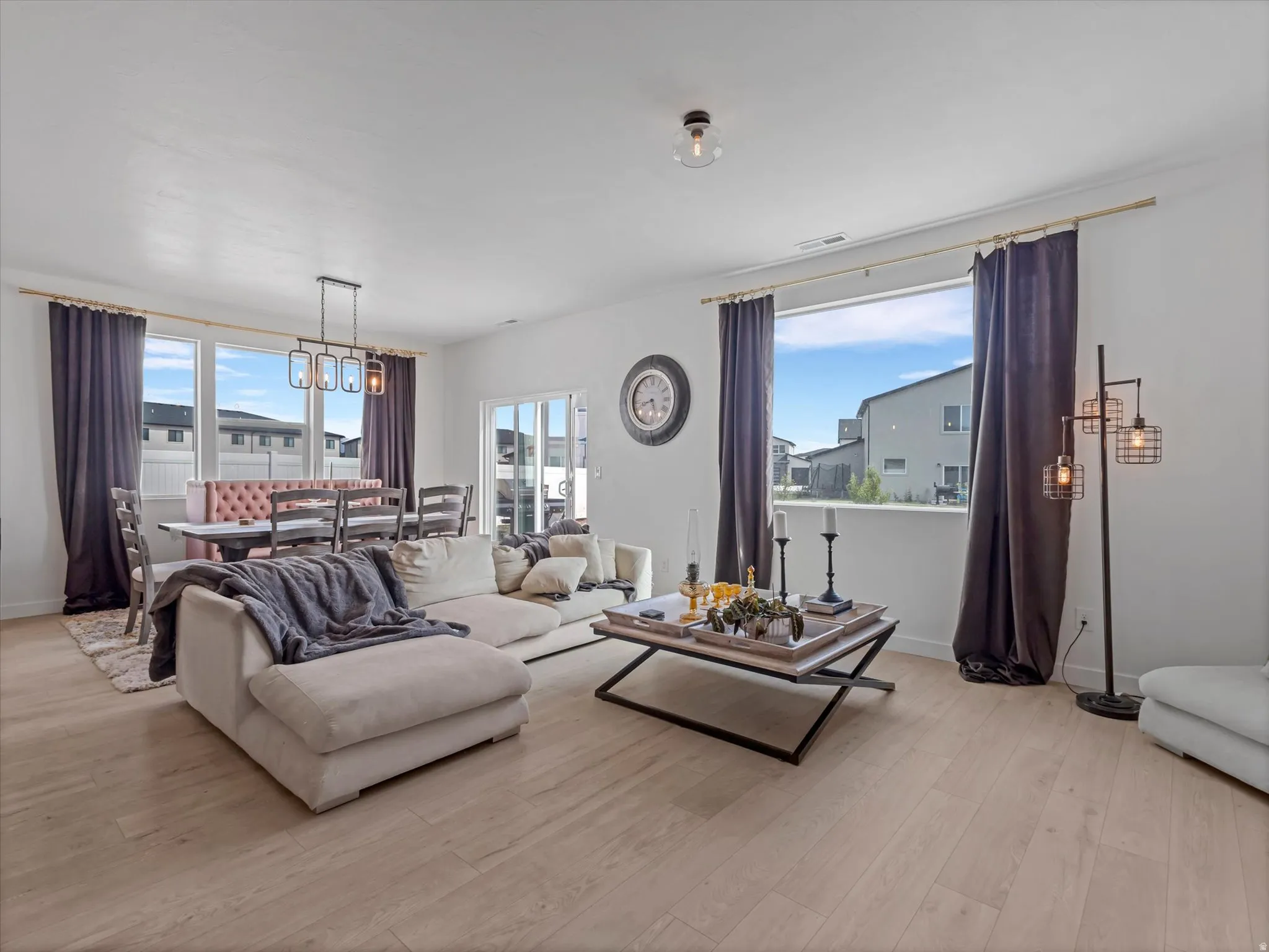 Open-concept living area featuring a dining nook with bench seating, wood-finish flooring, a contemporary chandelier, large windows with curtain rods, and recessed lighting