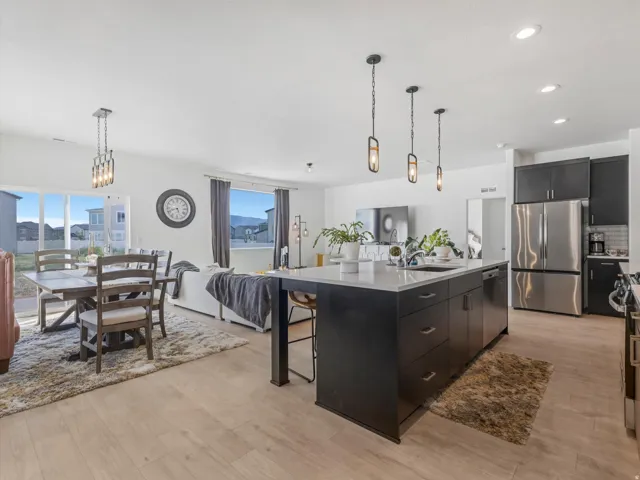 Open concept living area featuring a kitchen island with seating, pendant lighting, stainless steel appliances, and wood-finish flooring
