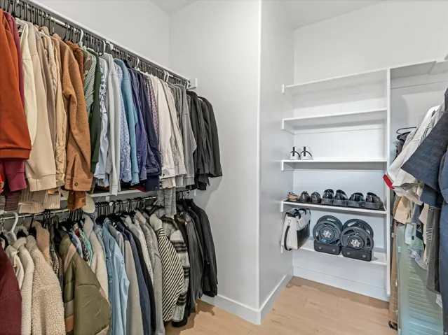 Custom closet organization featuring multiple hanging rods, built-in shelving, light wood-finish flooring, and white walls