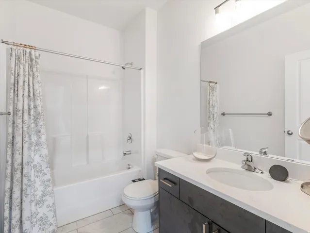 Bathroom featuring a white tub/shower combination, a dark wood-finish vanity with a white countertop and integrated sink, a large wall-mounted mirror, and tile flooring