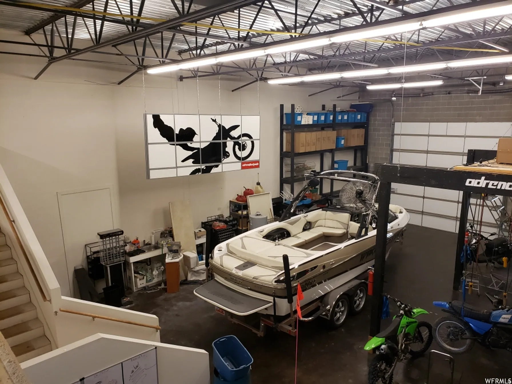 Spacious warehouse interior featuring a high, open-truss ceiling, overhead fluorescent lighting, and a roll-up garage door