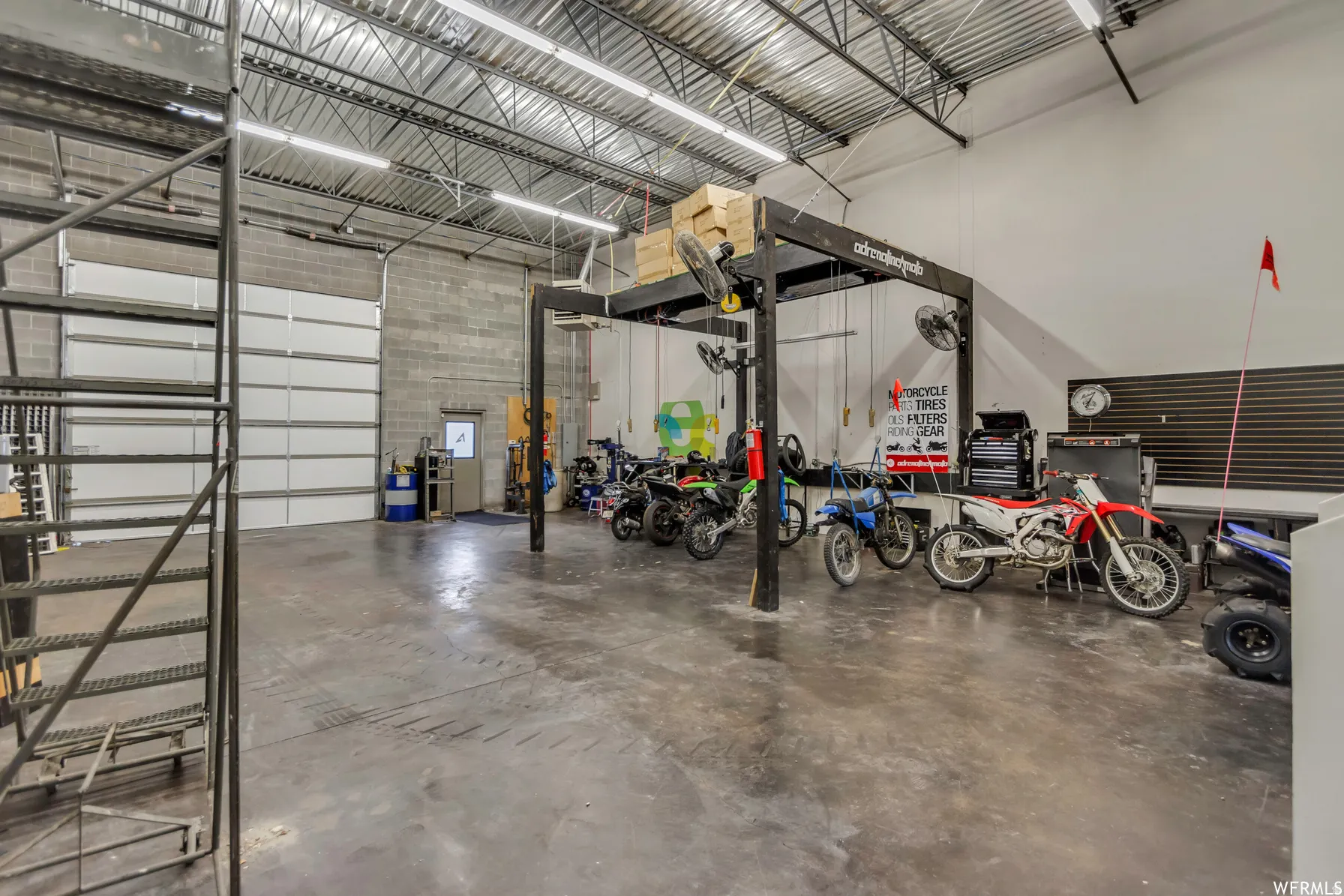Spacious industrial-style garage featuring a large overhead door, concrete block walls, exposed metal truss ceiling, and concrete flooring