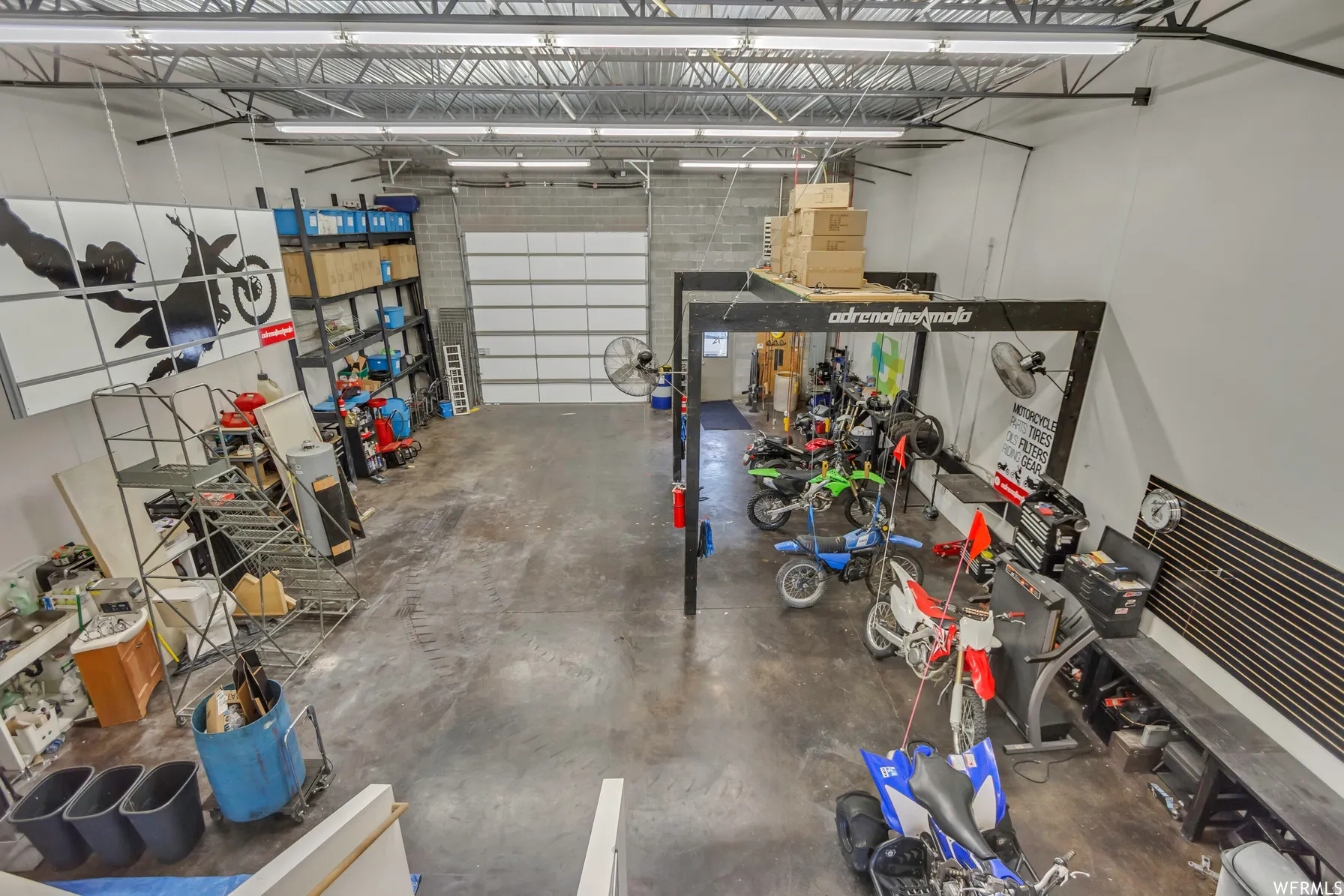 Spacious commercial interior featuring high ceilings with exposed trusses, concrete flooring, and a large white overhead door