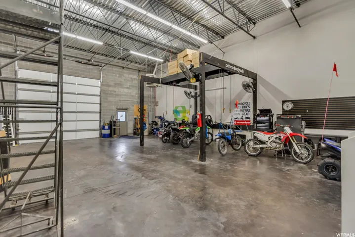 Spacious industrial-style garage featuring a large overhead door, concrete block walls, exposed metal truss ceiling, and concrete flooring