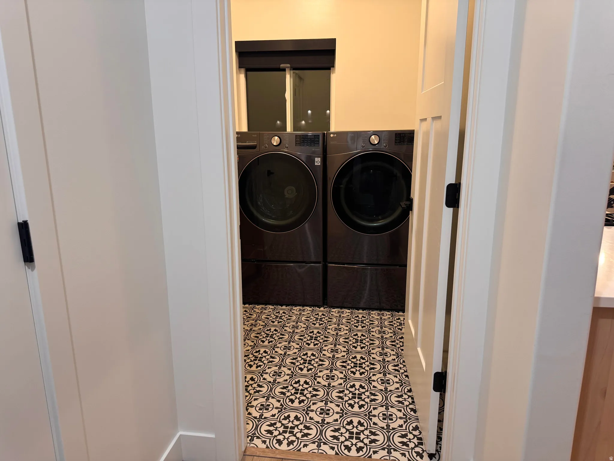 Laundry area featuring patterned tile flooring, a window with a dark roller shade, and white paneled interior doors