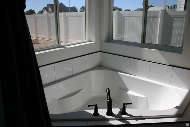 Corner soaking tub featuring matte black fixtures, surrounding white tile, and a bright window