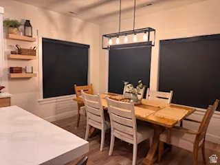 Dining area featuring wood-finish flooring, a linear chandelier, and three windows with dark roller shades