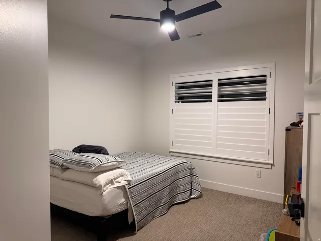 Room featuring a ceiling fan, white wall paint, and white plantation shutters on the window