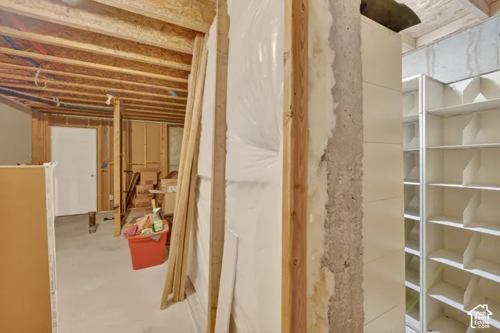 Unfinished basement space featuring exposed wood framing, concrete foundation walls, and integrated shelving units