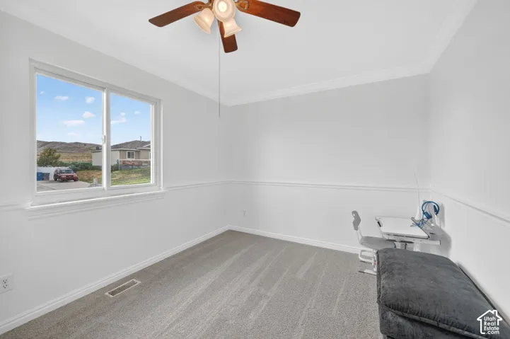 Bright interior room featuring a multi-pane window, crown molding, chair rail detailing, a ceiling fan with integrated lighting, and neutral carpeting