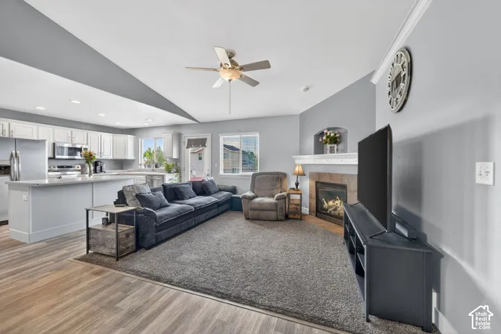 Open-concept living space featuring wood-finish flooring, a contemporary ceiling fan, and a gas fireplace with a stone surround and white mantel
