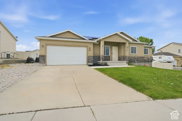 Stucco exterior with stone veneer accents, an attached garage, a concrete driveway, and a covered front porch entry
