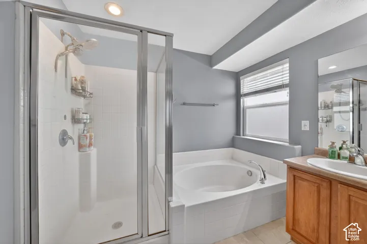 Bathroom featuring a glass-enclosed shower, built-in soaking tub, wood-finish vanity with a single basin sink, and tile flooring