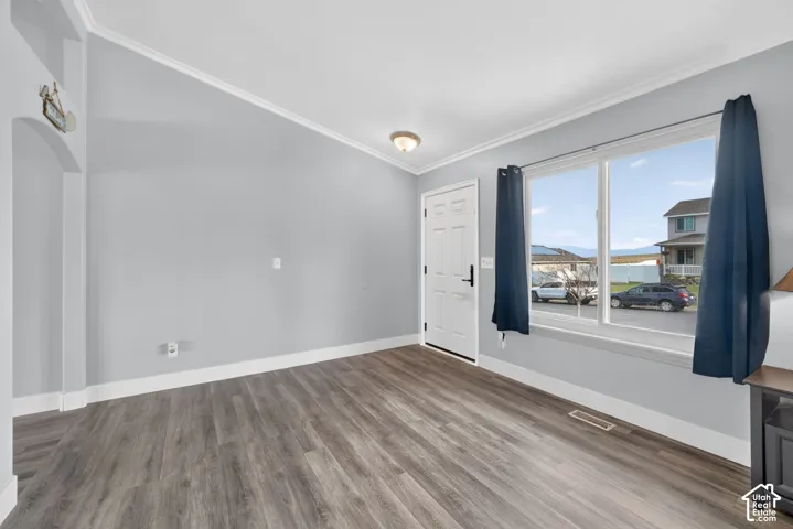 Spacious room featuring wood-finish flooring, light gray walls, white baseboards, and crown molding