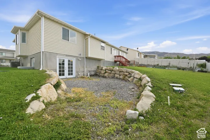 Exterior featuring a walk-out basement with double French doors, a gravel patio area, a rock retaining wall, and a sloped lawn