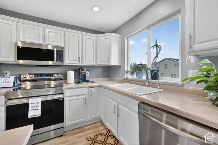 Kitchen featuring white cabinetry, stainless steel appliances, light-toned countertops, a double basin sink, and a large window