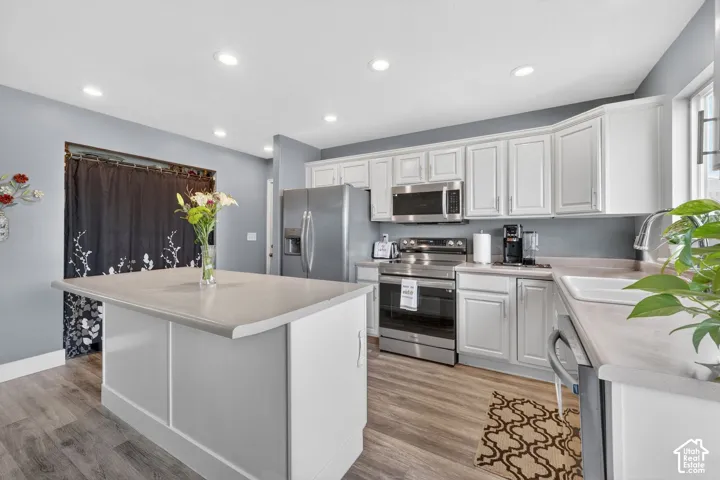 Kitchen featuring a central island with a light-toned countertop, white cabinetry, stainless steel appliances, and wood-finish flooring