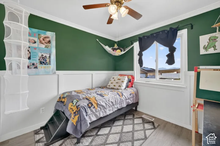 Bedroom featuring a ceiling fan with integrated lighting, wood-finish flooring, and white crown molding