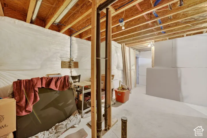 Unfinished basement space featuring exposed wood joists, concrete flooring, and white insulation