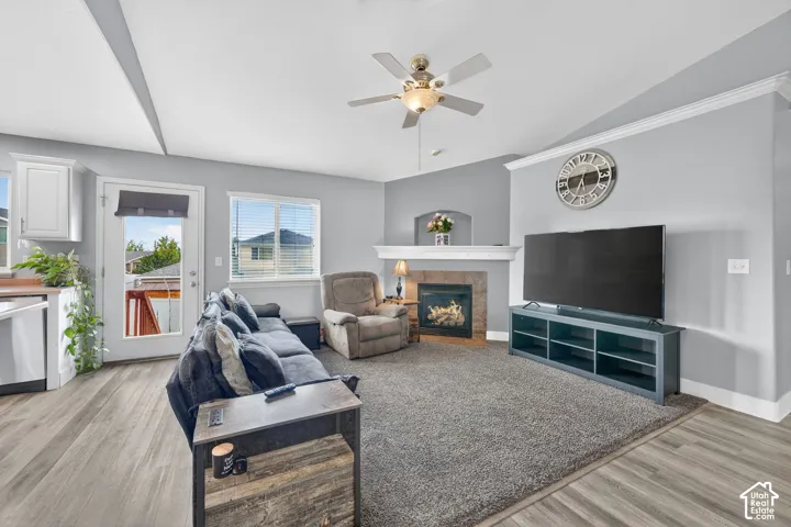 Spacious living area featuring wood-finish flooring, a ceiling fan, crown molding, and a fireplace with a stone surround