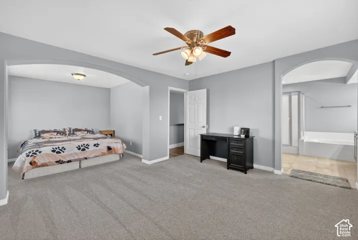 Spacious carpeted room featuring a ceiling fan with light, arched doorways, an alcove with recessed lighting, and an attached bath with a built-in tub and glass-enclosed shower