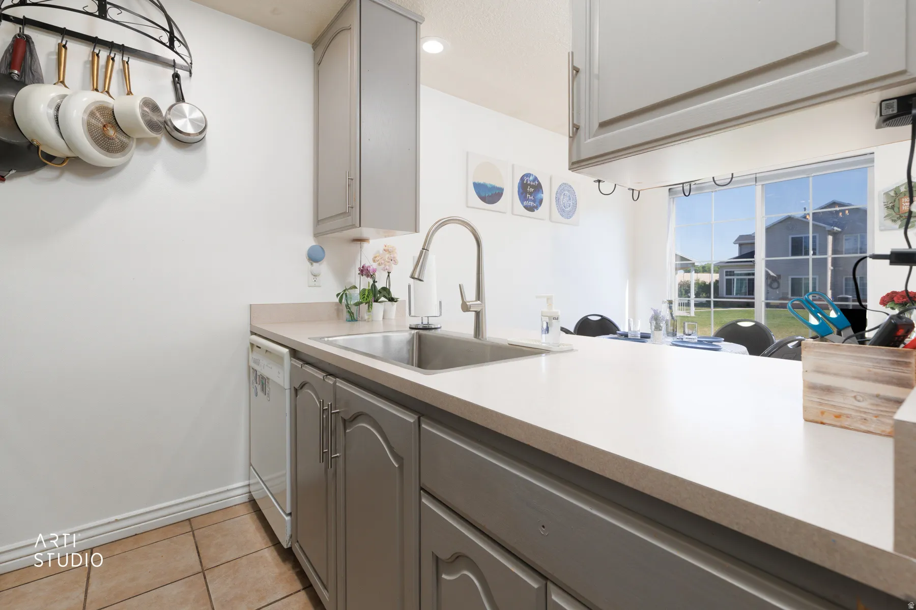 Kitchen featuring a stainless steel sink with a gooseneck faucet, light-toned countertops, gray cabinetry, and tile flooring