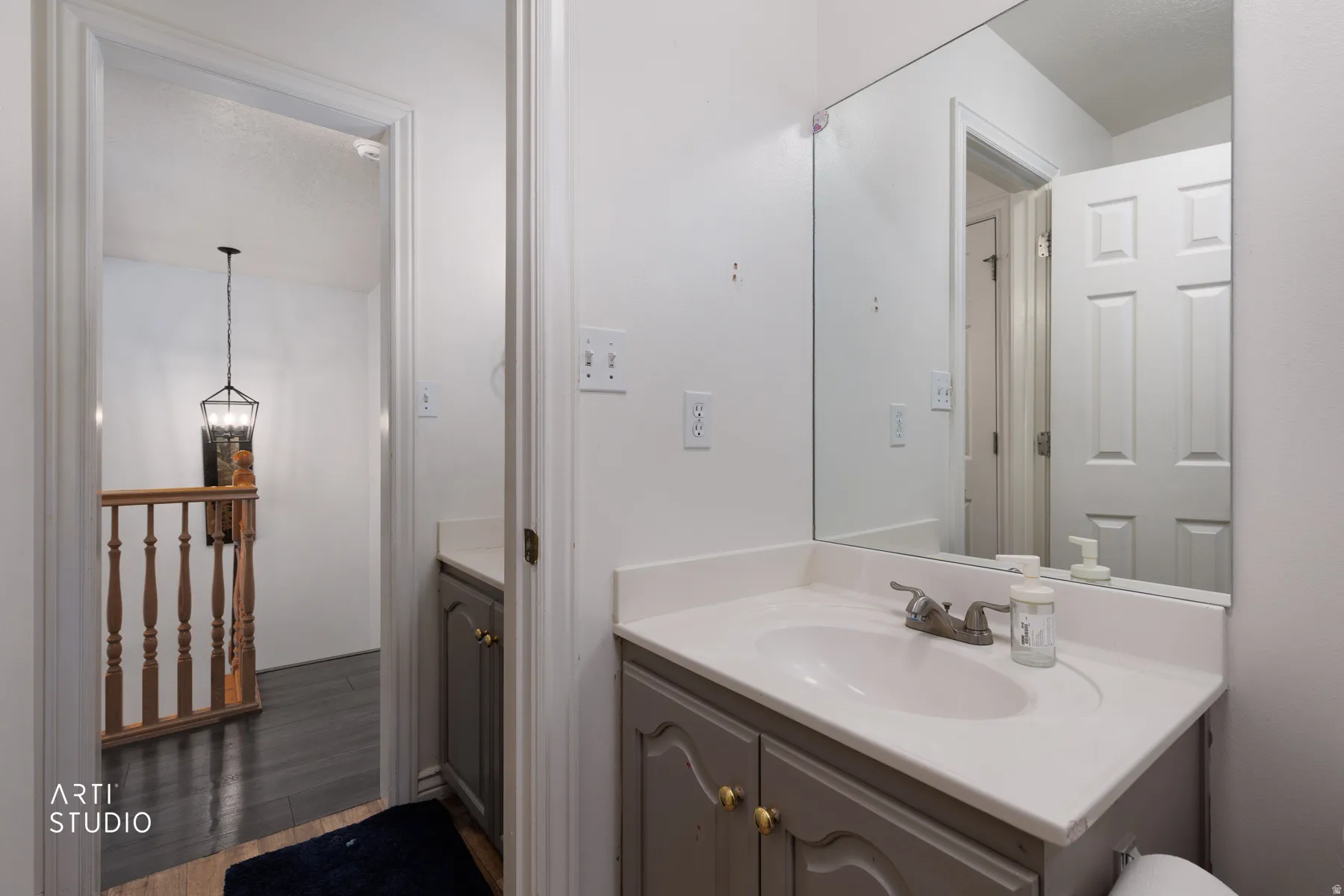 Bathroom vanity featuring a single basin sink, light-colored countertop, and gray cabinetry with gold-toned hardware
