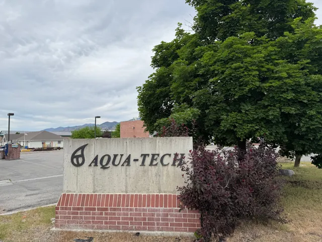 Brick and concrete monument sign with dark lettering, surrounded by mature trees and shrubs