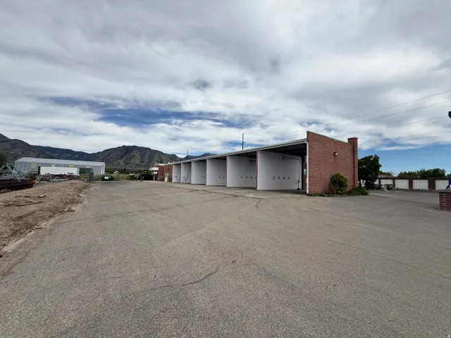 Spacious paved lot featuring multiple bays with roll-up doors, brick construction, and an expansive mountain backdrop