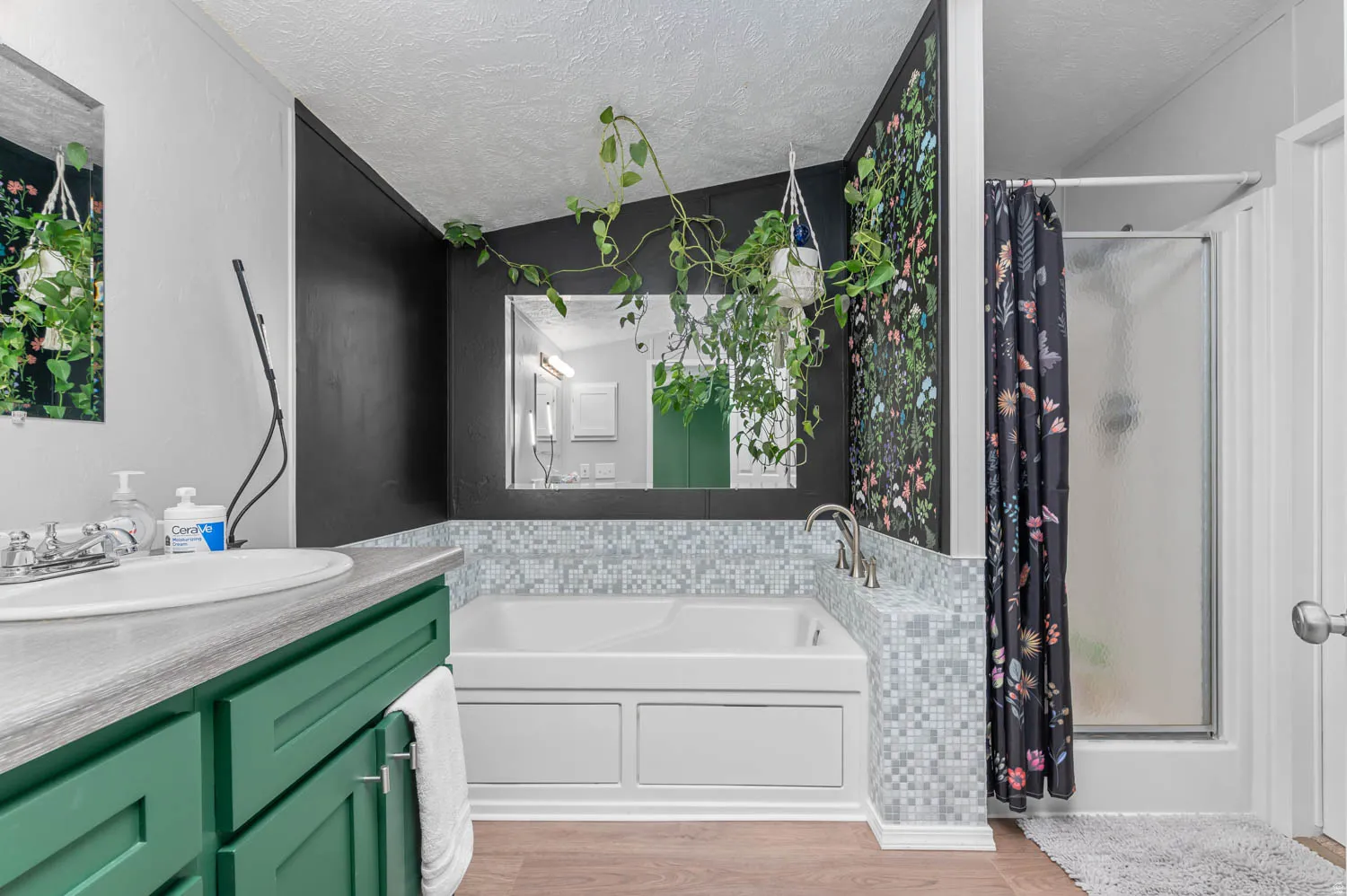 Bathroom featuring a built-in tub with mosaic tile surround, a separate shower enclosure, a vanity with a green cabinet base and integrated sink, and wood-finish flooring