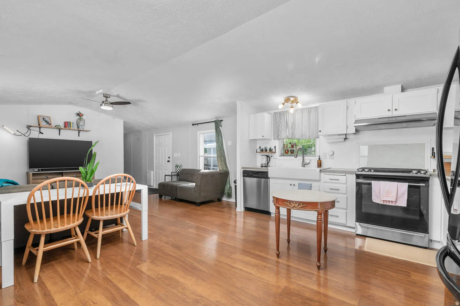 Open-concept living space featuring wood-finish flooring, white kitchen cabinetry, stainless steel appliances, a farmhouse sink, and a ceiling fan